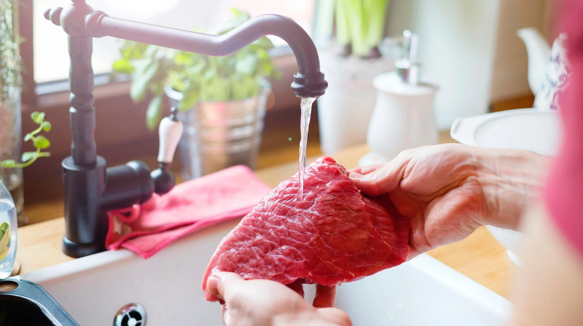 Руки миють сире мясо під водою в кухонній раковині