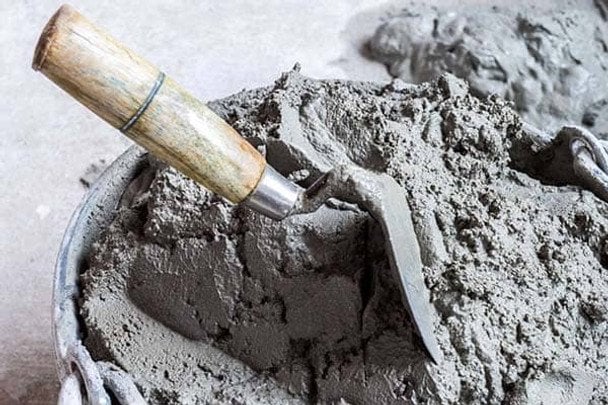Кельма з деревяною ручкою у відрі з свіжим цементним розчином