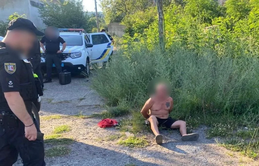 Поліцейські біля патрульного авто та чоловік без сорочки сидить на землі