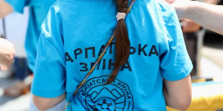 Дівчинка ззаду у синій футболці з написом Карпатська зміна та логотипом