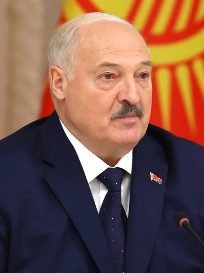 Олександр Лукашенко у синьому костюмі біля мікрофона на тлі білоруського прапора