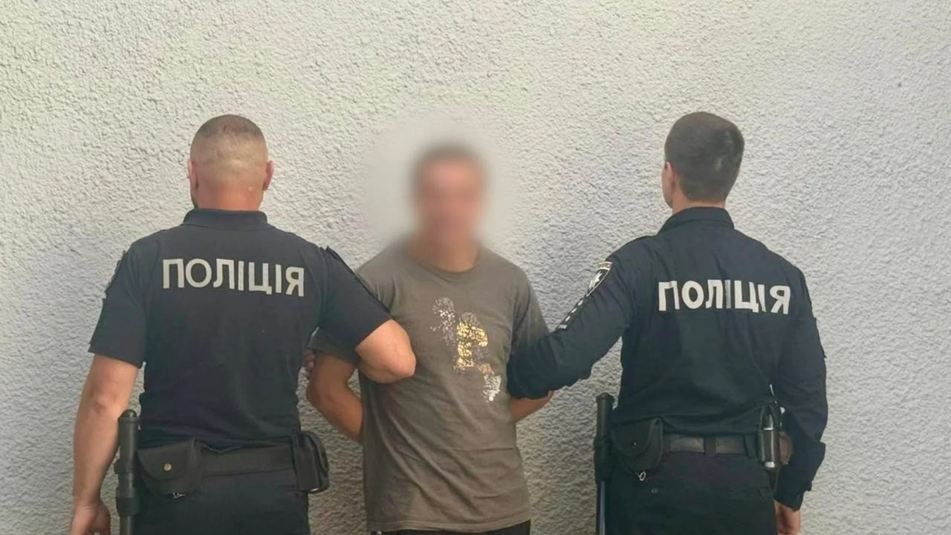 Двоє поліцейських тримають чоловіка з розмитим обличчям біля стіни