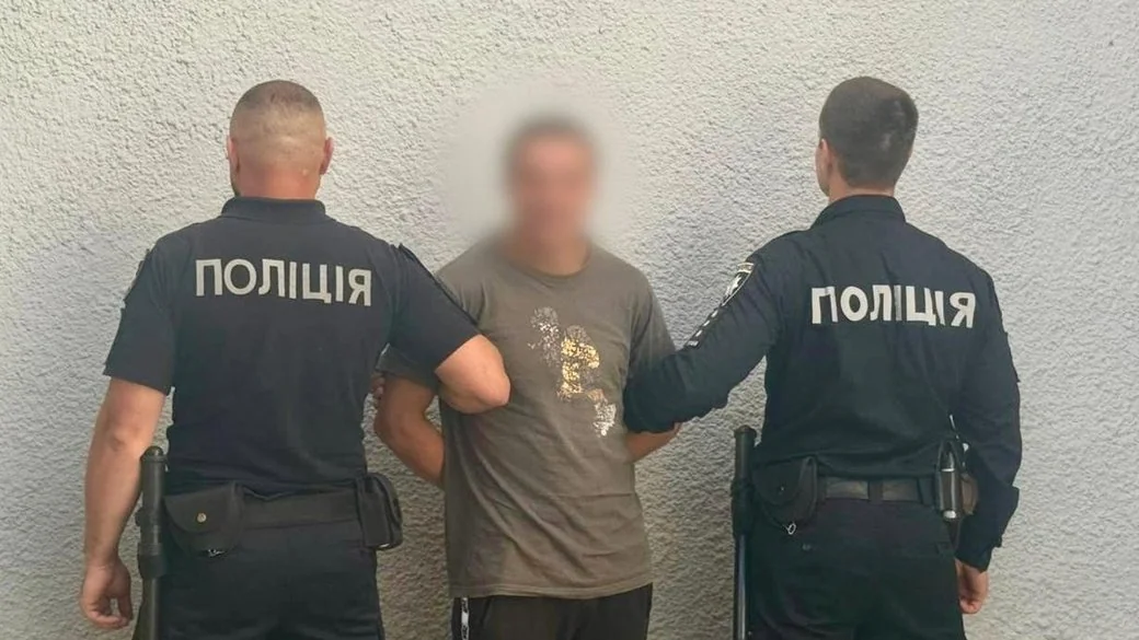 Двоє поліцейських тримають затриманого чоловіка з розмитим обличчям біля стіни