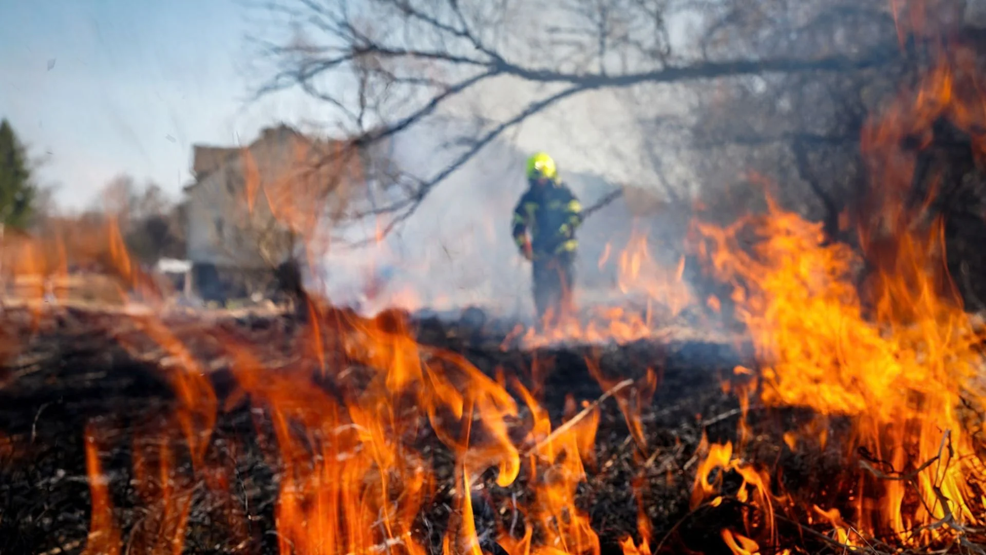 Пожежник у жовтій касці стоїть серед палаючого сухостою і диму
