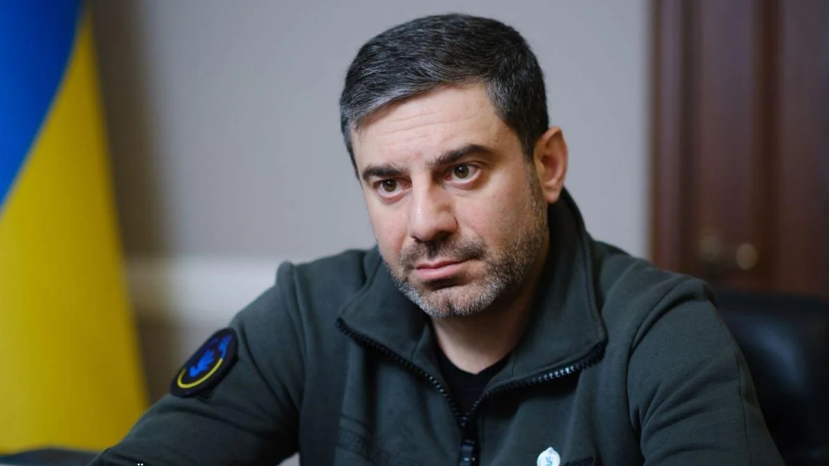 Дмитро Лубінець у зеленому флісі сидить біля українського прапора