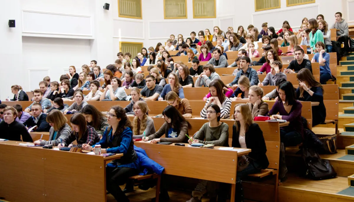 Студенти сидять рядами у великій лекційній аудиторії з дерев’яними партами