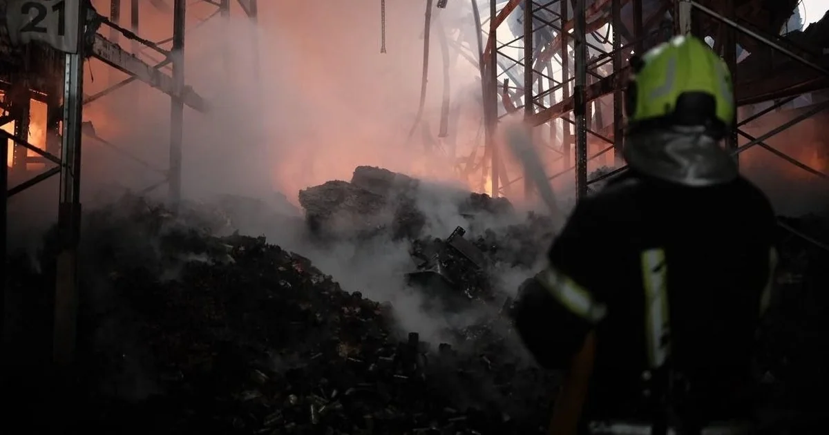 Пожежник у жовтій касці оглядає тліючі руїни зруйнованої будівлі після атаки