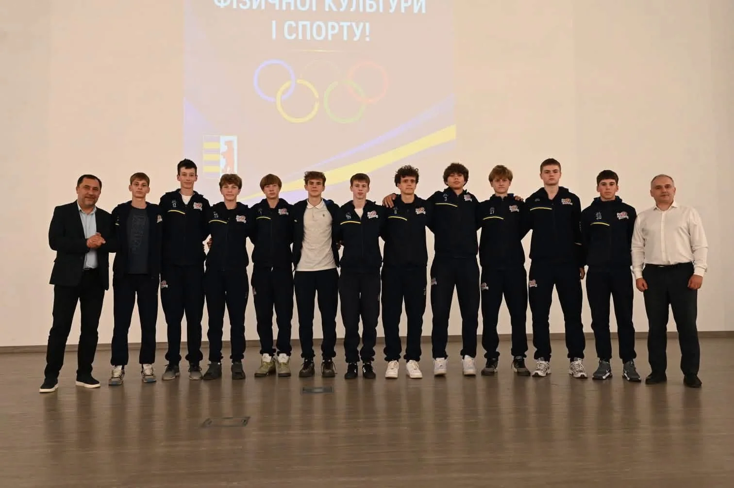 Юні спортсмени в синіх костюмах на сцені з олімпійськими кільцями