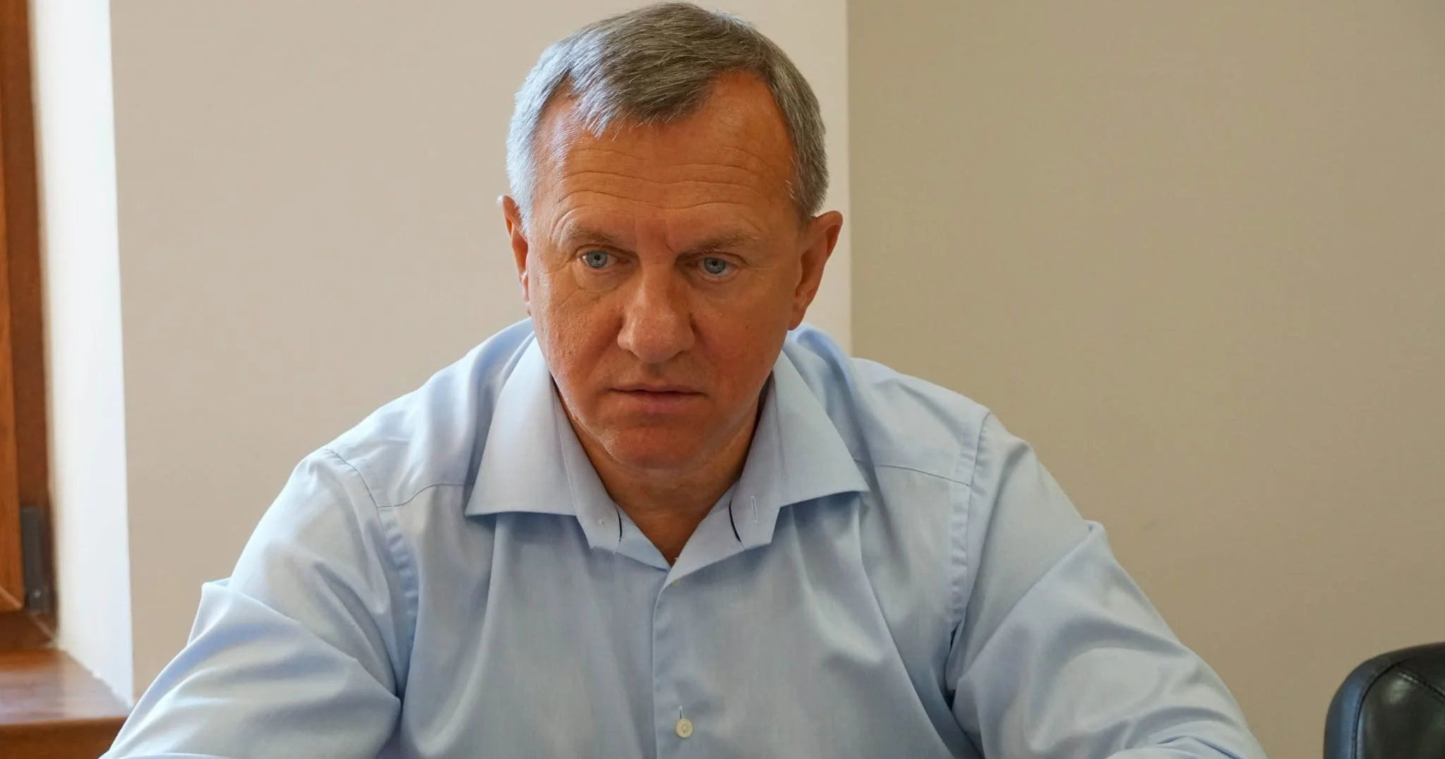 Сивоволосий чоловік у блакитній сорочці сидить за столом у кабінеті