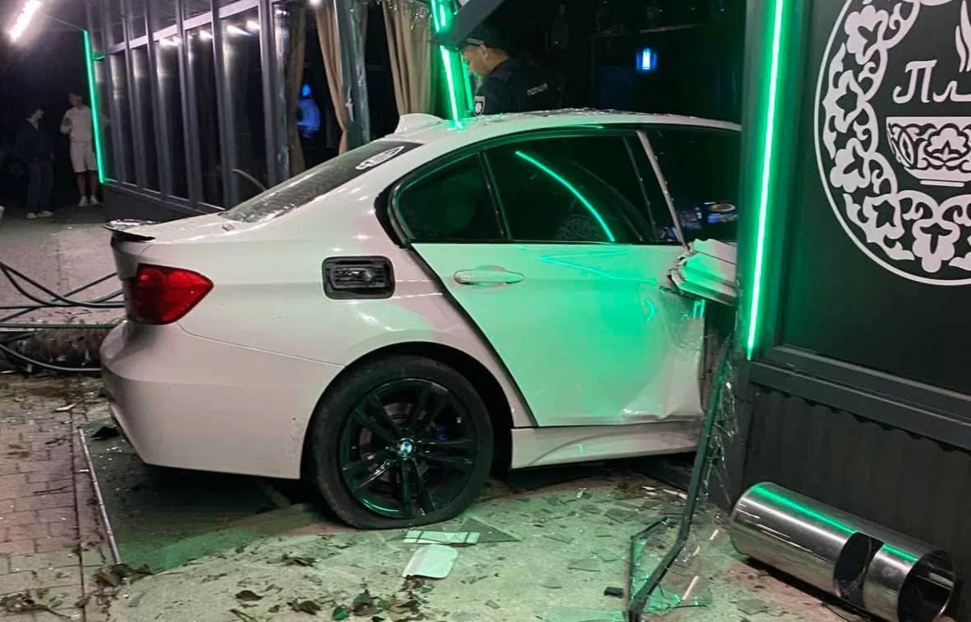 Біла BMW врізалася у вітрину закладу з зеленим неоном вночі