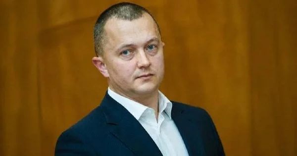 Чоловік у темному піджаку та білій сорочці на дерев’яному тлі