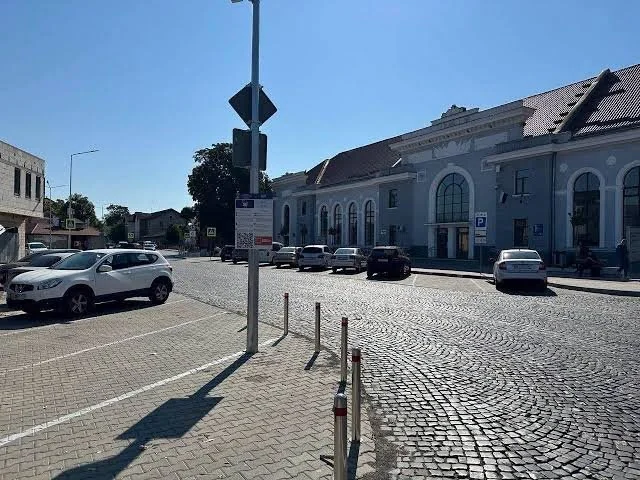 Автомобілі на брукованій парковці біля сірої будівлі з арками