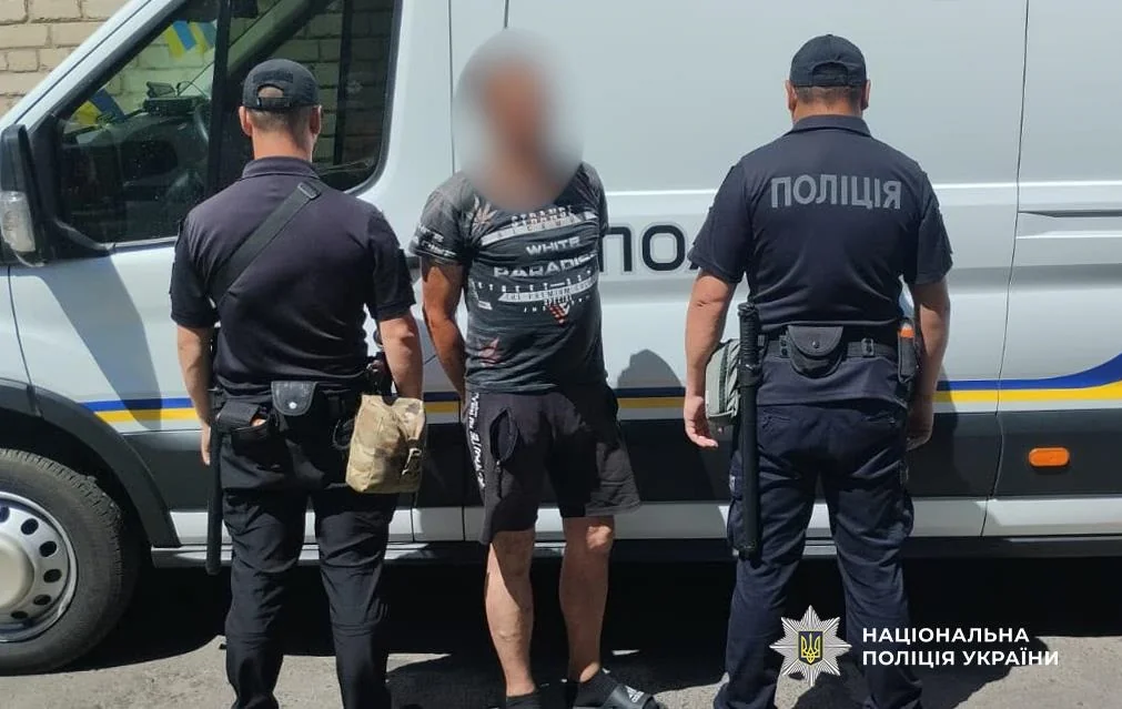 Двоє поліцейських стоять із затриманим біля білого мікроавтобуса поліції
