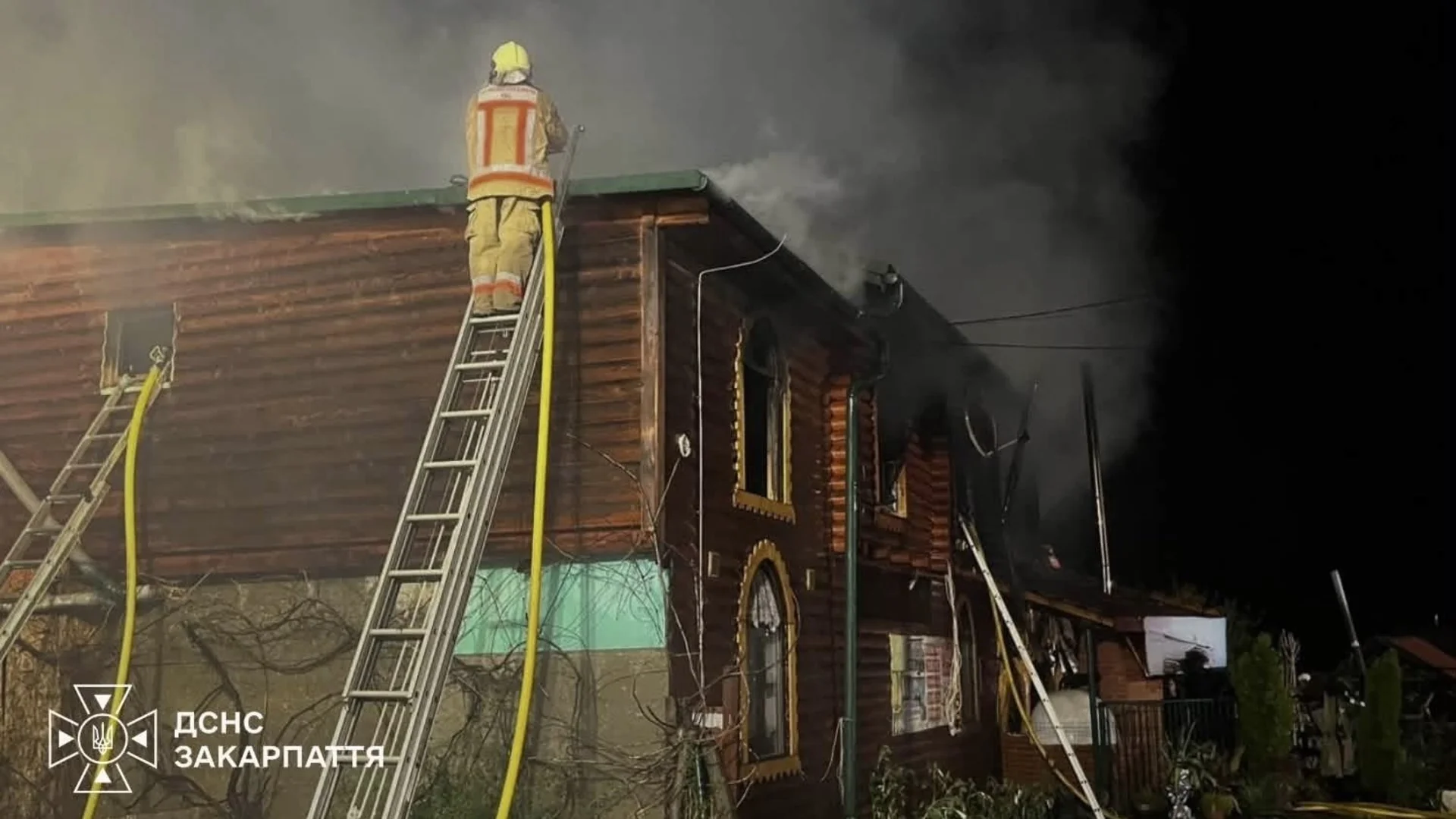 Рятувальник на драбині гасить пожежу дерев’яного будинку вночі