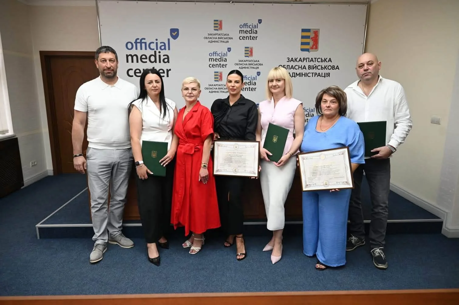Сім фахівців ЦНАПів із грамотами перед банером медіацентру Закарпатської ОВА
