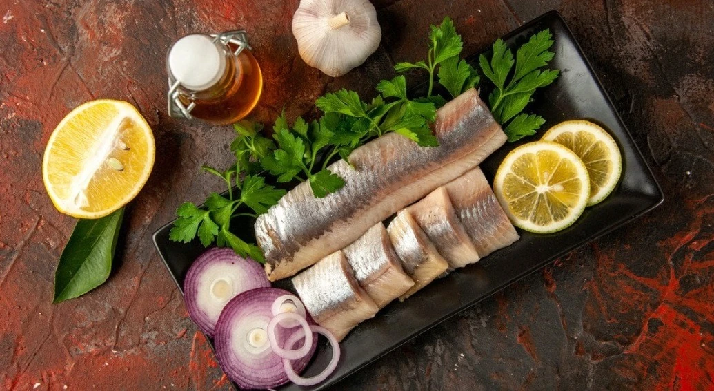 Нарезанная сырая атлантическая скумбрия с лимоном и зеленью на черной доске