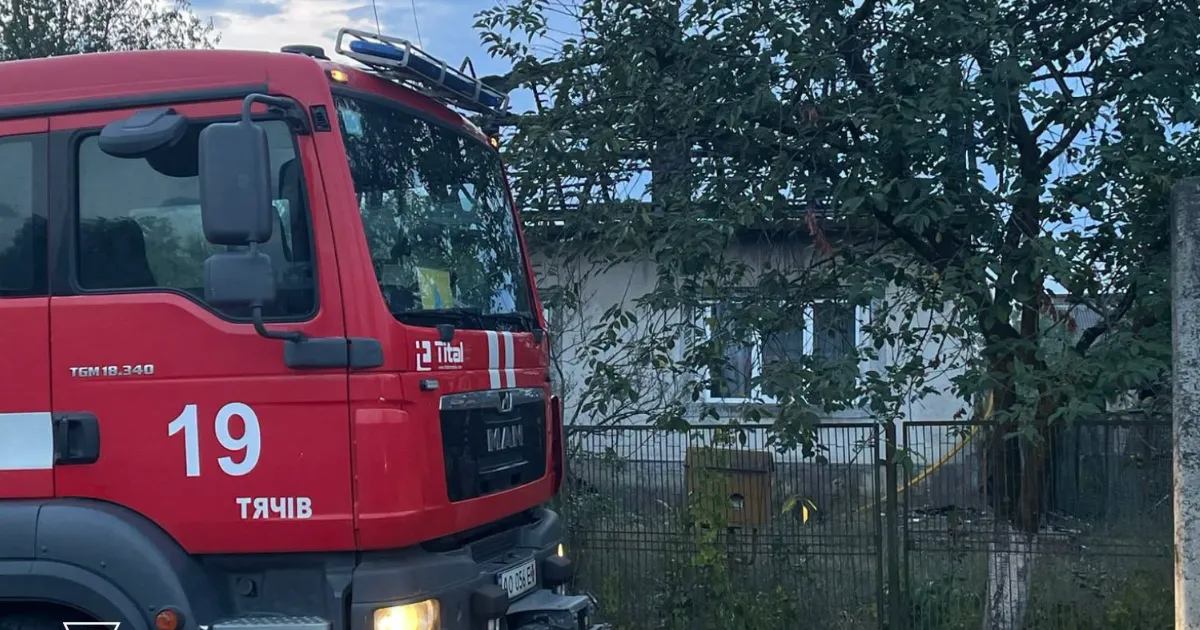Червоний пожежний автомобіль Тячева біля сільського будинку за парканом