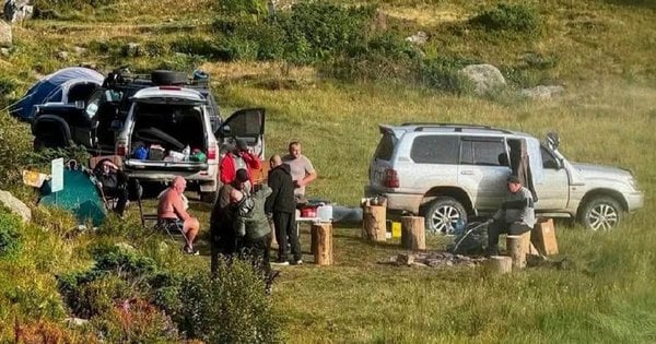 Група чоловіків біля двох позашляховиків і наметів на гірській галявині